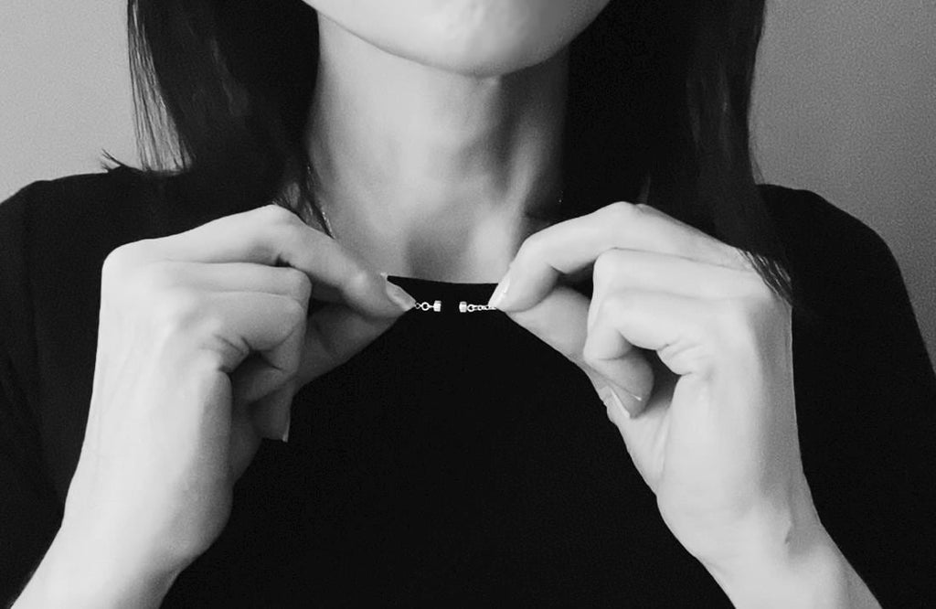 Two hands bringing the halves of the magnetic clasp together at the front of the neck, closing it without a catch.