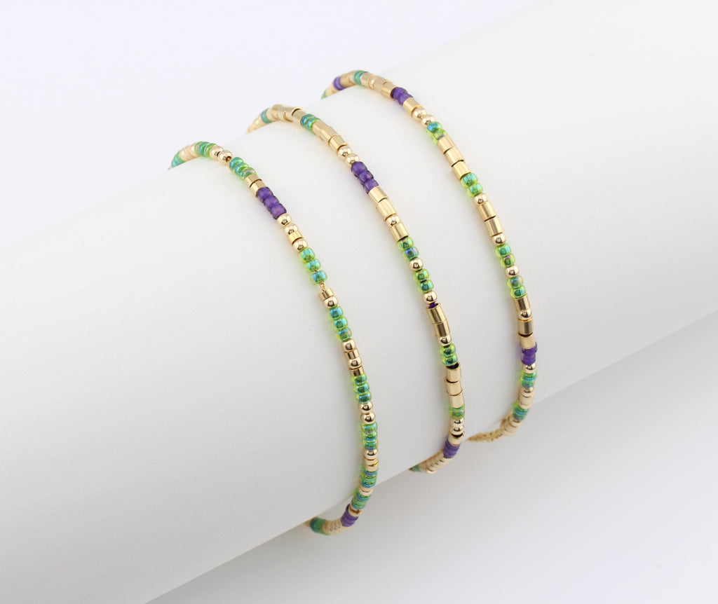 Three 14k gold fill morse code bracelets in green and purple beads, draped over a white cylinder