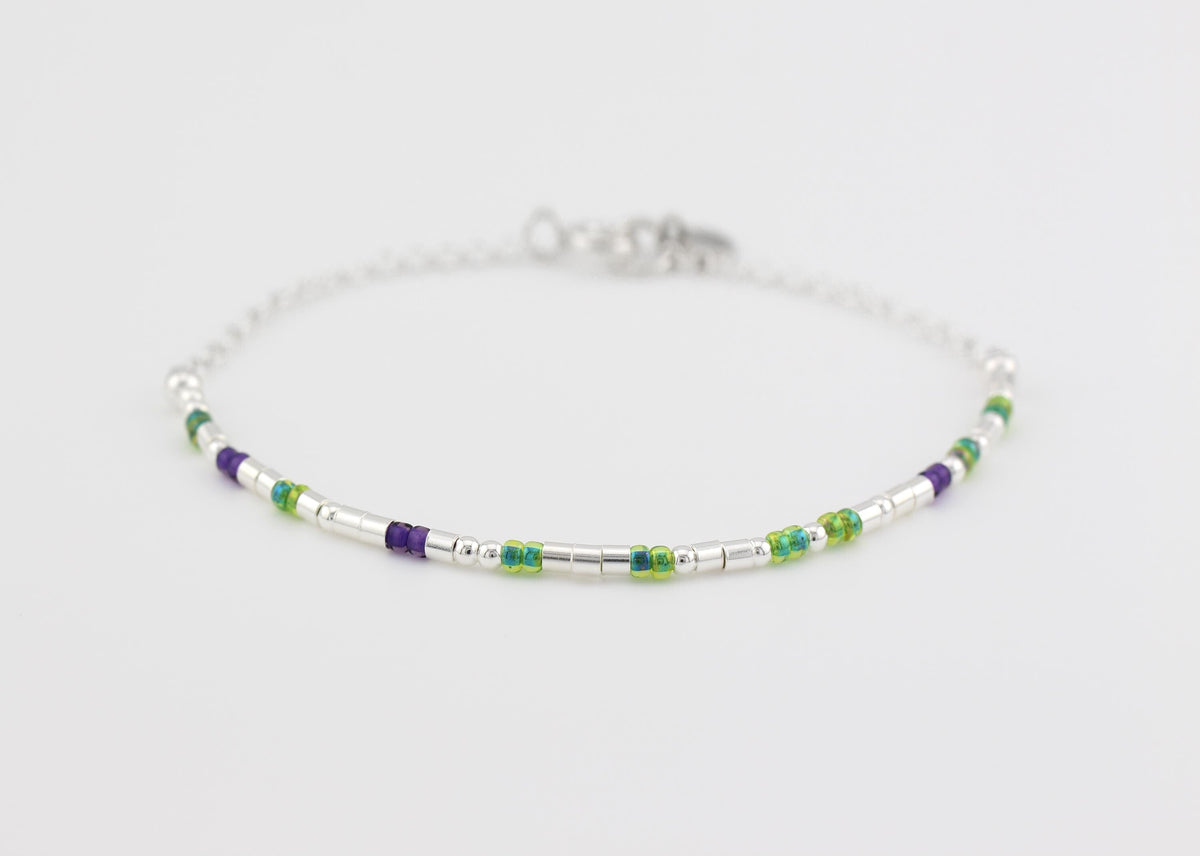 Sterling silver morse code bracelet with green and purple glass beads laid flat, spring ring clasp and gifted. tag visible