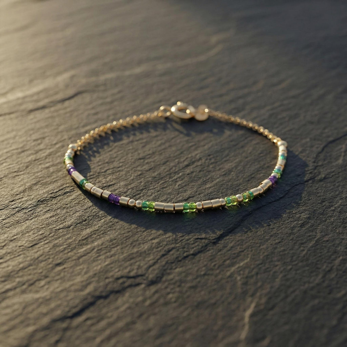 Sterling silver morse code bracelet with green and purple beads on dark slate