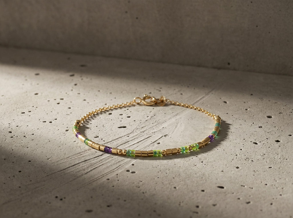 14k gold fill morse code bracelet with green and purple beads curled on grey concrete