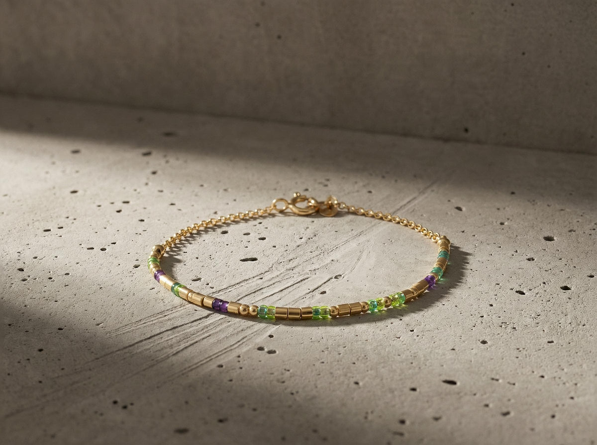 14k gold fill morse code bracelet with green and purple beads curled on grey concrete