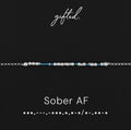 Sober AF spelled in Morse code in glass and metal beads, shown on black