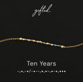 Ten Years spelled in Morse code in glass and metal beads, shown on black