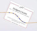 Dodged a Bullet spelled in Morse code on a beaded bracelet, shown on its printed gift card