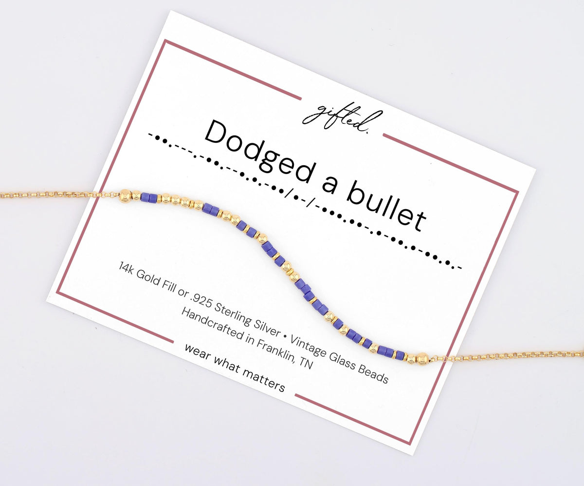 Dodged a Bullet spelled in Morse code on a beaded bracelet, shown on its printed gift card