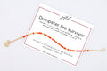 Dumpster Fire Survivor spelled in Morse code on a beaded bracelet, shown on its printed gift card